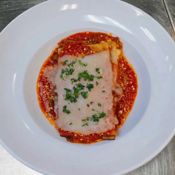 A serving of Sal's Famous Pizzeria's lasagna, topped with melted cheese, red sauce, and parsley.