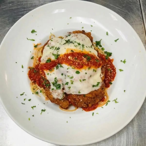 Chicken Parmesan with melted mozzarella, marinara sauce, and parsley, served over spaghetti on a white plate.