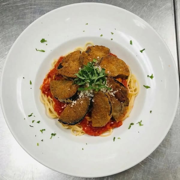 Spaghetti with red sauce topped with breaded eggplant slices, fresh basil, and grated cheese.