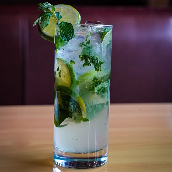 Refreshing mojito cocktail with ice, lime slices, and mint leaves on a wooden table.