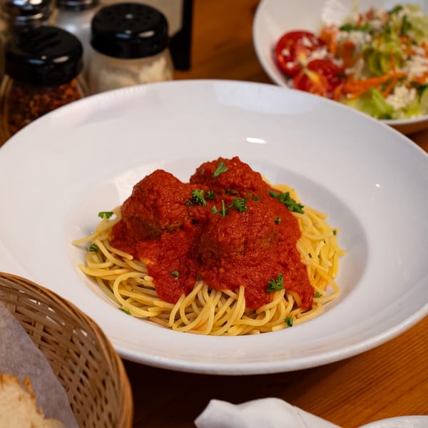 Spaghetti and meatballs with red sauce and parsley, with a side salad and bread.