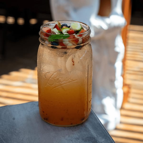 A refreshing fruit punch in a mason jar, garnished with strawberries, blueberries, lime, and mint.