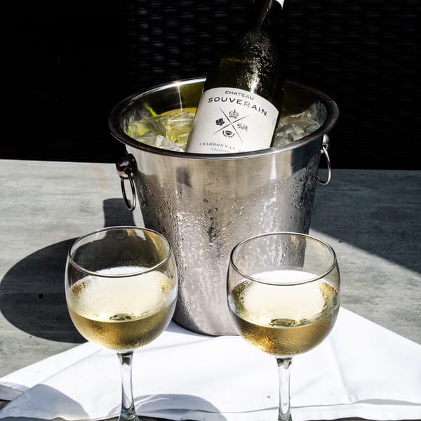 Chilled white wine bottle in an ice bucket with two glasses of wine on a white napkin.