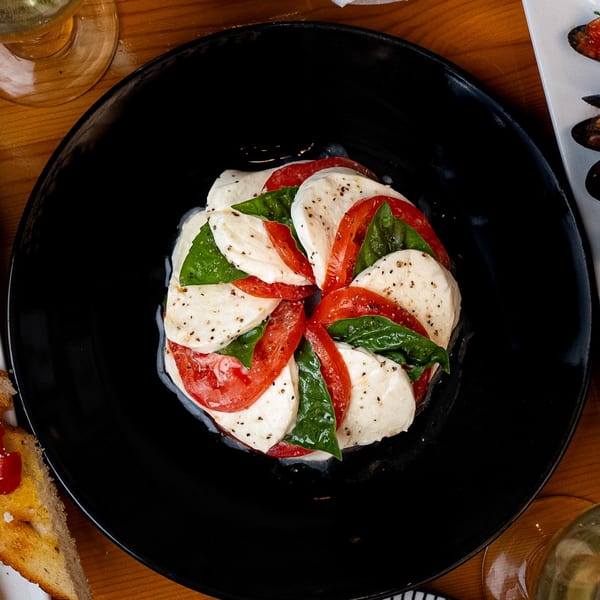 Caprese salad with sliced mozzarella, tomatoes, and basil, drizzled with dressing on a black plate.