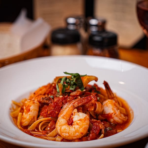 Close-up of shrimp linguine with red sauce and basil in a white bowl.