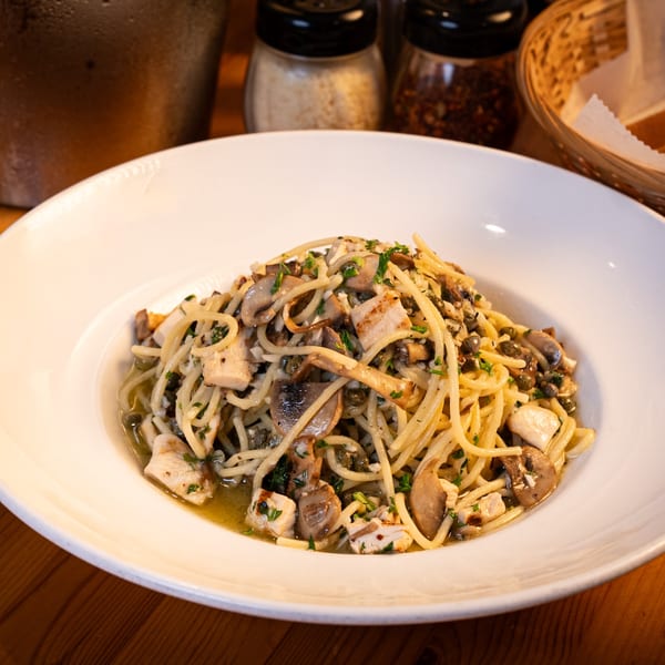 Spaghetti with mushrooms, chicken, and capers in a light sauce, served in a white bowl.