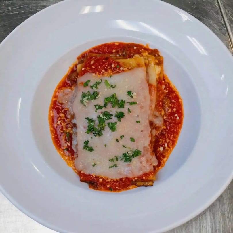 A serving of Sal's Famous Pizzeria's lasagna, topped with melted cheese, red sauce, and parsley.