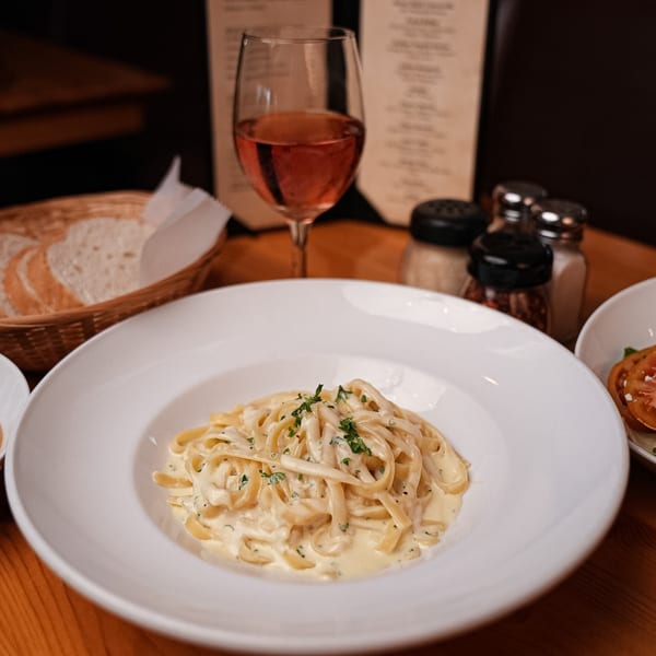 Creamy fettuccine alfredo with parsley, a glass of rosé, bread, and spices on a wooden table.