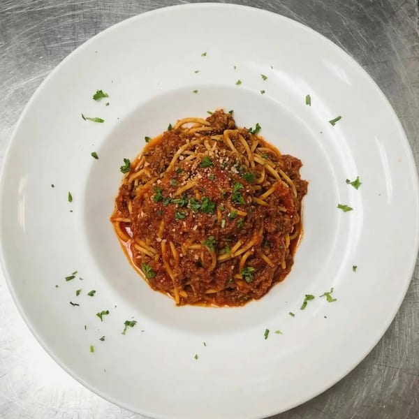 A white plate of spaghetti bolognese with meat sauce, parmesan cheese, and fresh parsley.