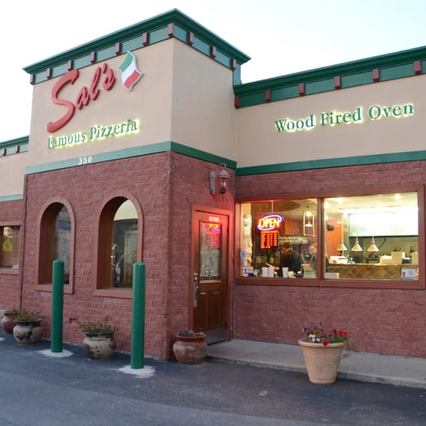 Exterior of Sal's Famous Pizzeria, a brick building with an "OPEN" sign and visible kitchen.