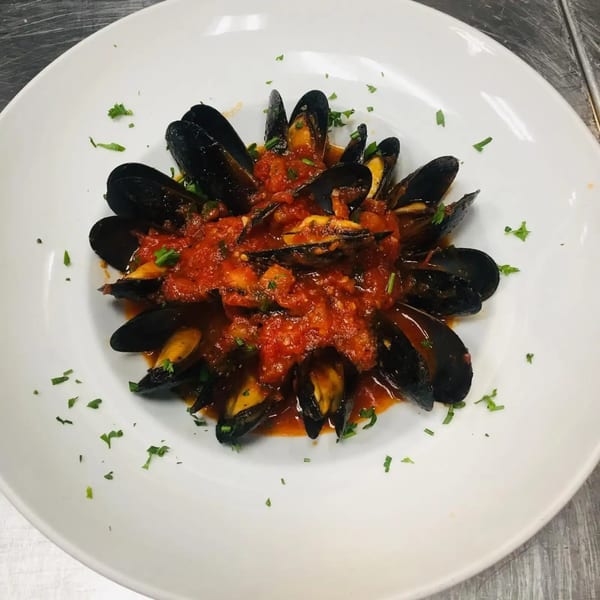 Mussels in a rich red tomato sauce, garnished with fresh herbs, served on a white plate.