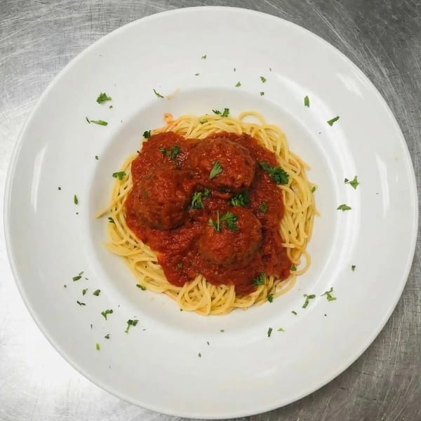 Spaghetti with meatballs and marinara sauce, garnished with parsley, on a white plate.