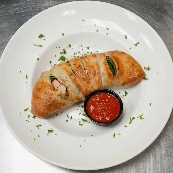 A golden-brown calzone with visible chicken and spinach filling, served with a side of marinara sauce.